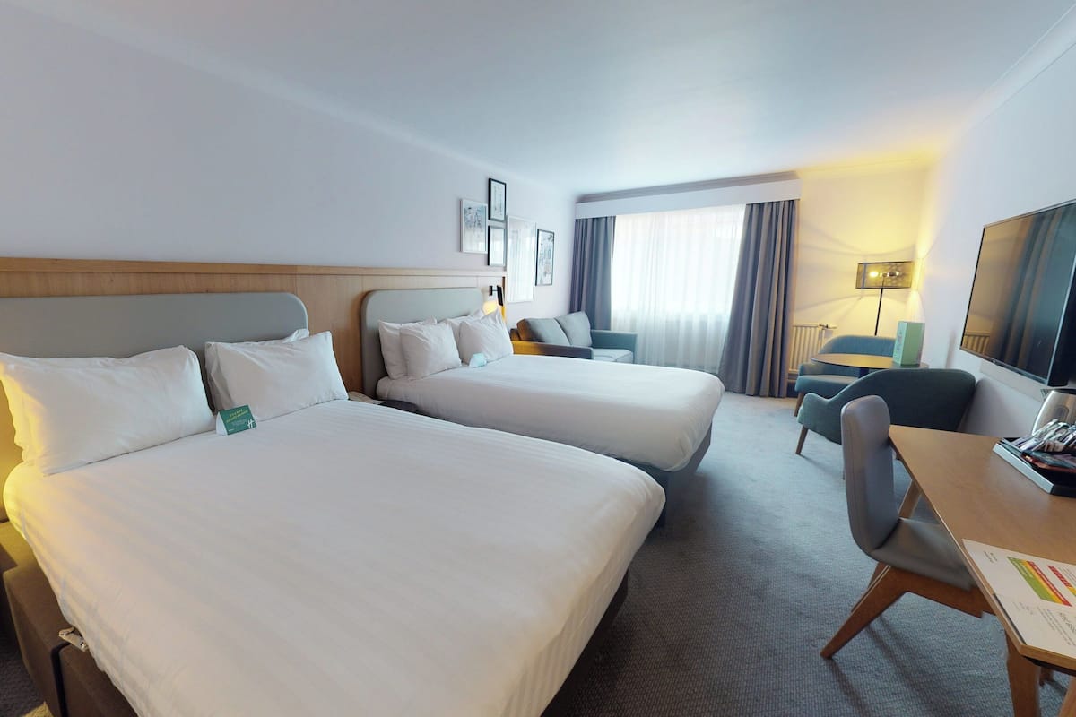 A hotel room with two beds, a desk, a chair, a TV, and a window with curtains.