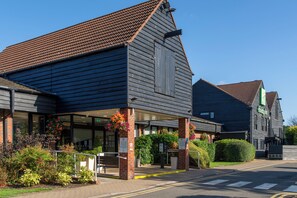 A building with a dark wooden facade, a tiled roof, and a covered entrance area with a bench and flower boxes.