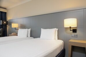 A hotel room with two beds, each with white linens, a bedside table with a lamp, and a wall-mounted phone.