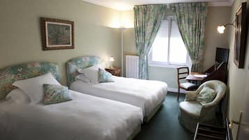 Una habitación con dos camas, un escritorio, una silla, una lámpara, un televisor y una ventana con cortinas.