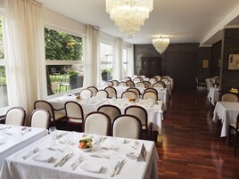 Un comedor formal con varias mesas dispuestas para el servicio, ventanas amplias y un candelabro.