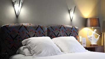 Habitación de hotel con cama, cabecera estampada, mesita de noche con lámpara y aplique de pared.