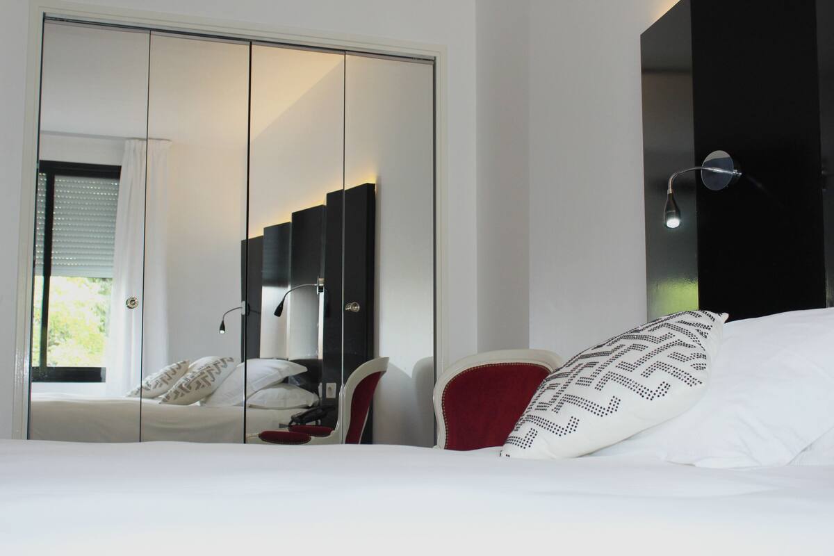 A bedroom with a bed, a red chair, a wardrobe, and a mirror.