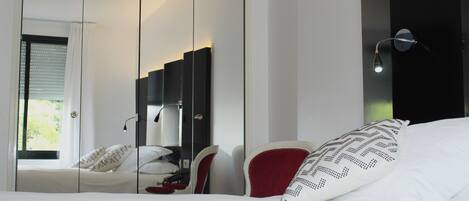 A bedroom with a bed, a red chair, a wardrobe, and a mirror.