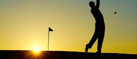 A silhouette of a golfer at sunset with a flag on a hill.
