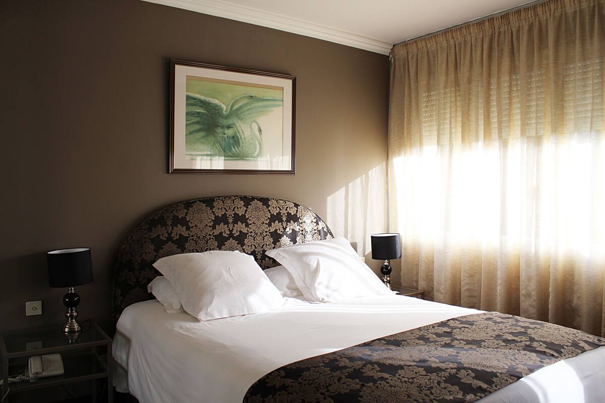 A neatly made bed with a floral headboard, a bedside lamp, and a framed artwork on the wall.