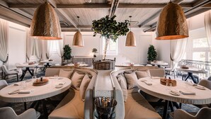 A modern dining area with round tables, cushioned seating, and hanging copper pendant lights. - Corinthia Palace Malta (Attard)