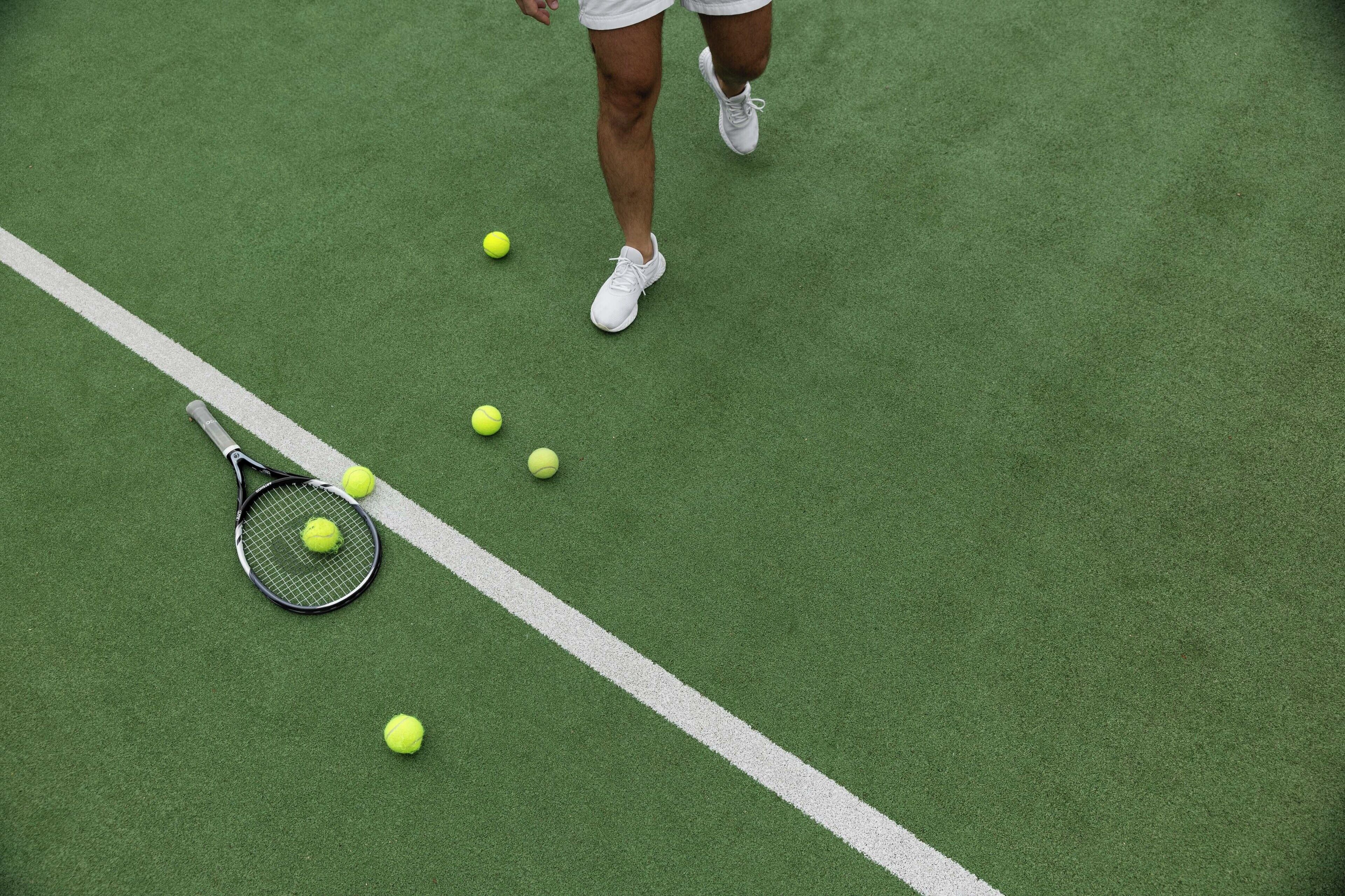 A tennis court with a net, a tennis racket, and several tennis balls.