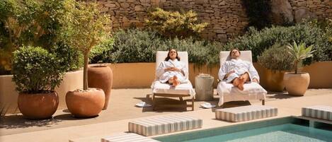 Zona junto a la piscina con sillones de descanso y plantas en macetas.