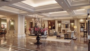 A spacious lobby with a marble floor, a central round table with floral arrangements, and a seating area with sofas and armchairs. - Corinthia Palace Malta (Attard)