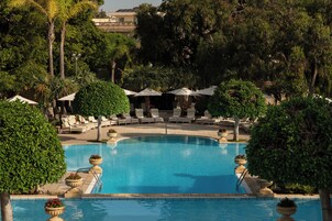 Zona de piscina con sillones de descanso y sombrillas, rodeada de árboles y follaje.