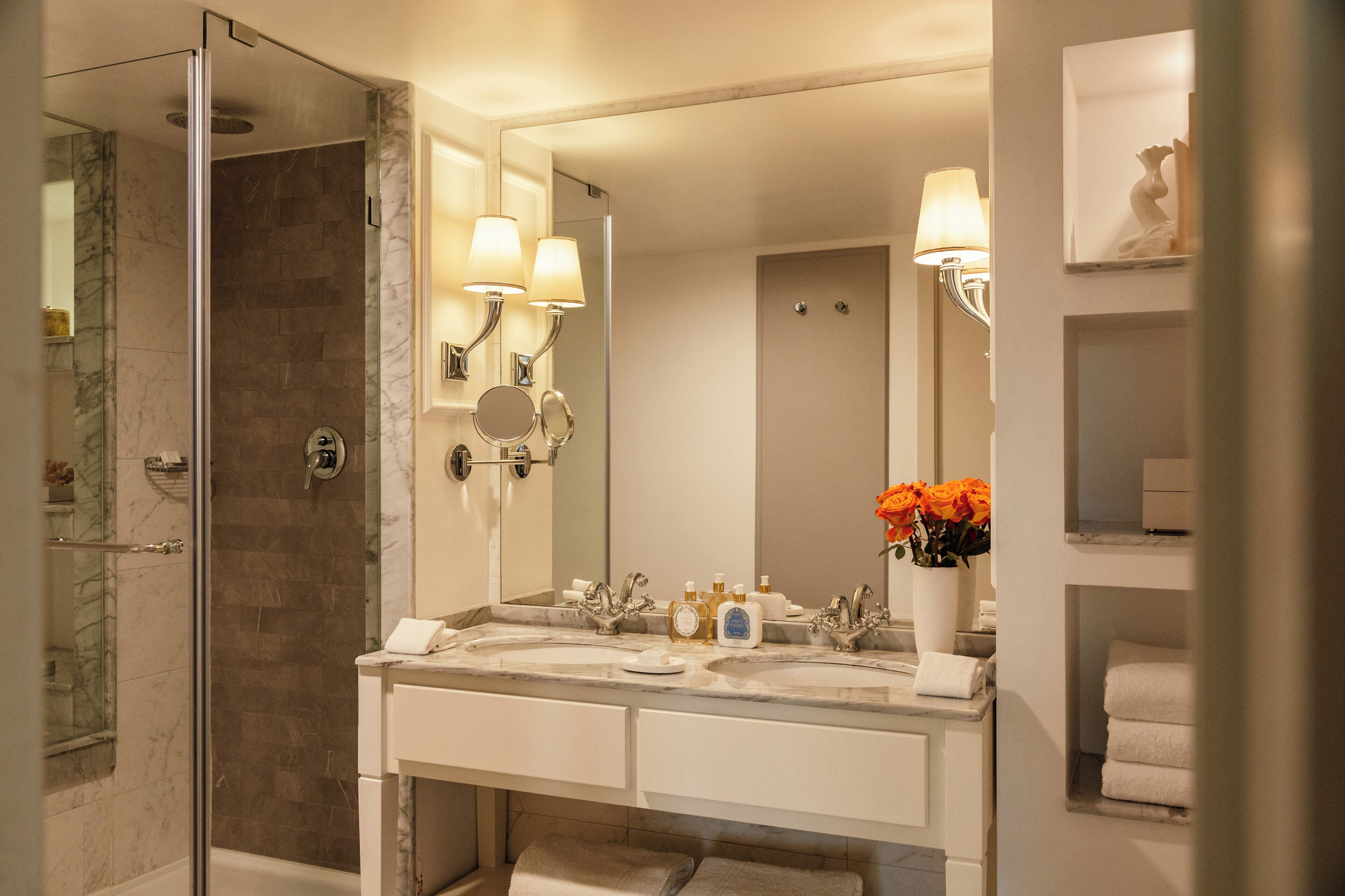 A modern bathroom with a glass-enclosed shower, a marble sink, and a large mirror with wall-mounted lights.