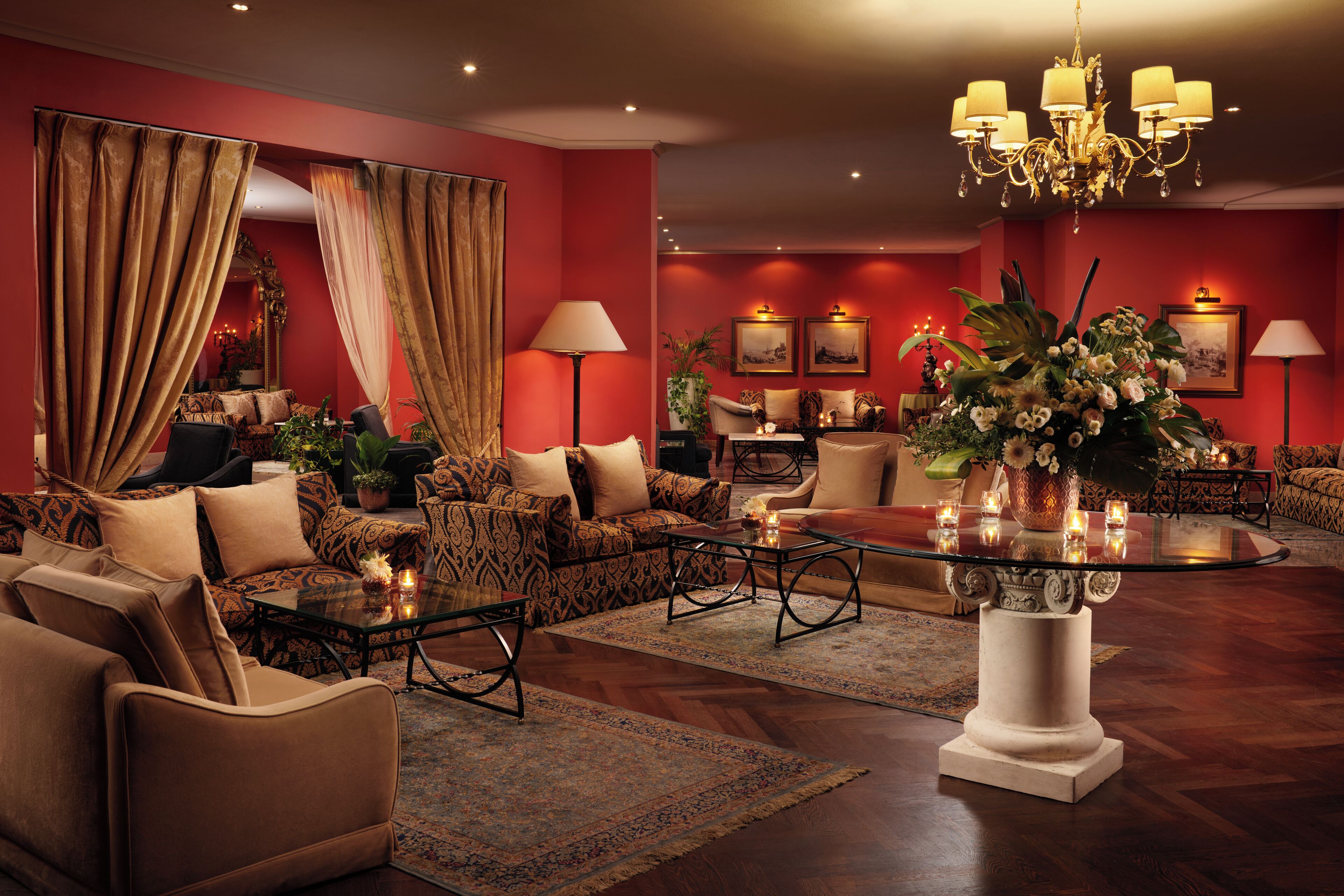 A luxurious living room with a red wall, a chandelier, and a coffee table with candles.