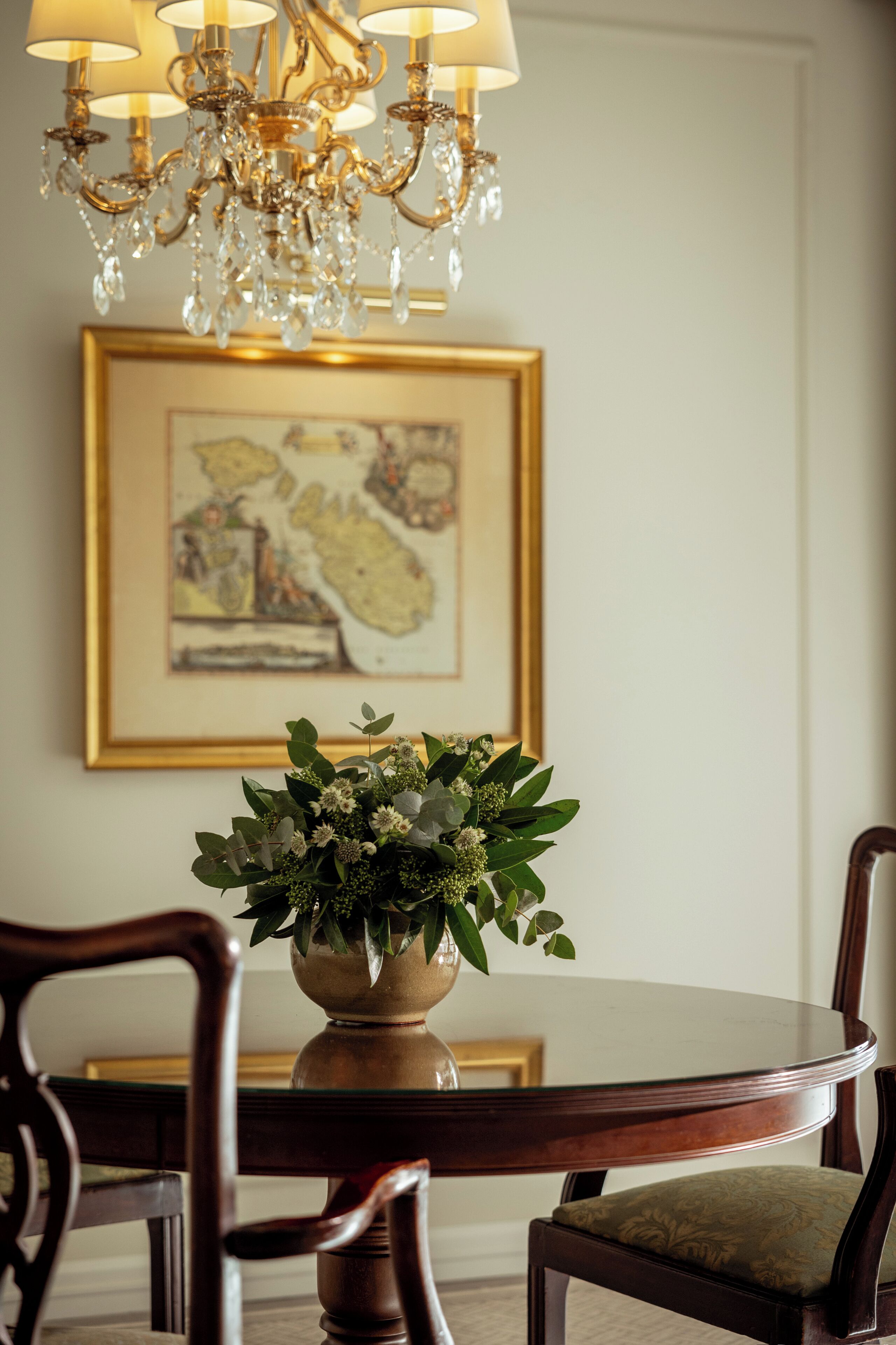 A dining area with a round table, chairs, a chandelier, and a framed map on the wall.