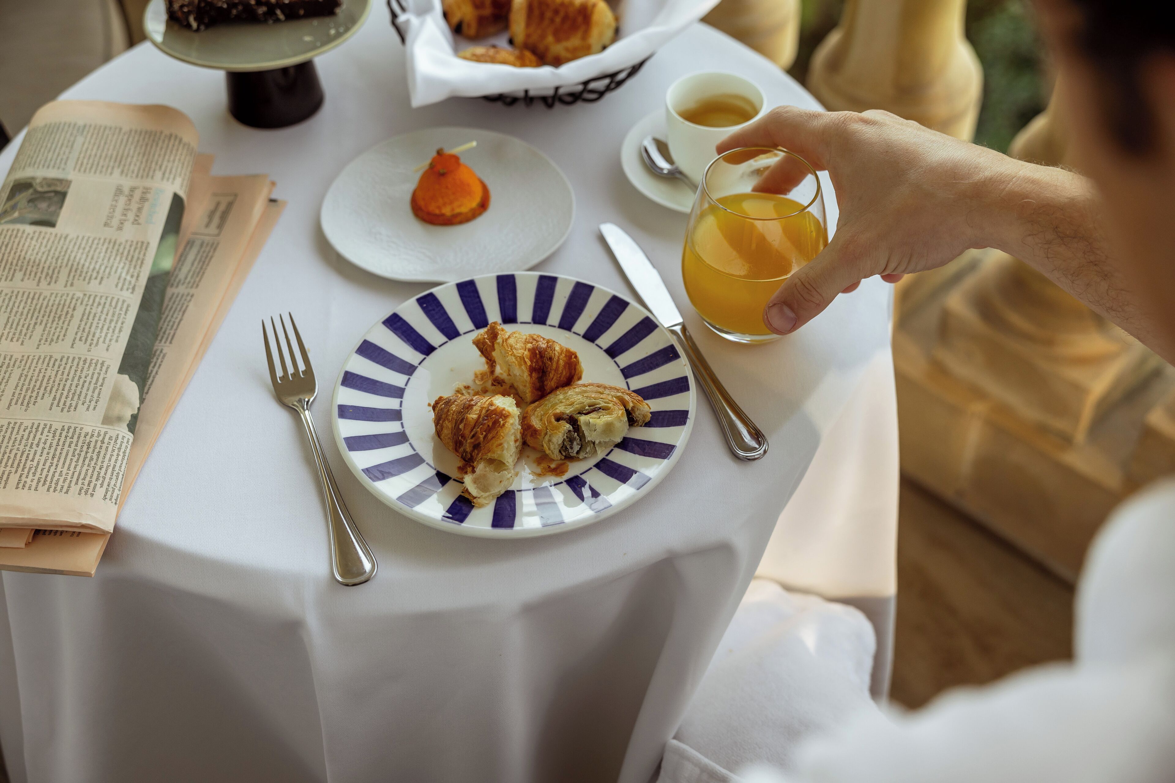 A table with croissants, a glass of orange juice, a cup of coffee, and a newspaper.