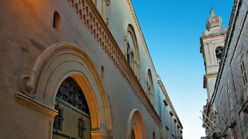 Una calle histórica con un edificio destacado que presenta arcos y una torre con campanas.