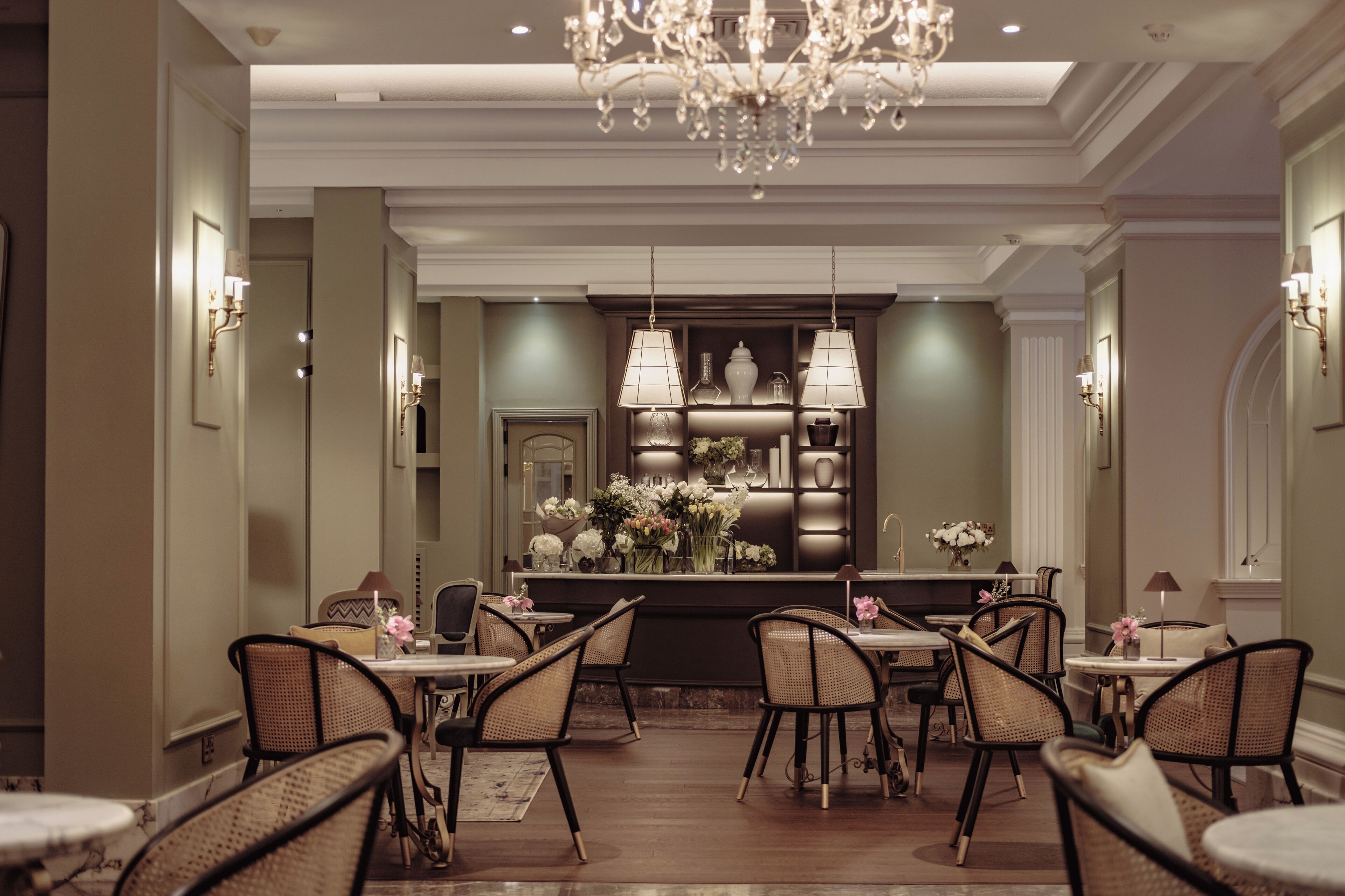 A formal dining area with a chandelier, wicker chairs, and a central table with a floral arrangement.