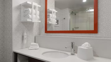 Une salle de bain moderne avec un grand miroir, un meuble de rangement pour les serviettes blanches, un lavabo et une cabine de douche en verre.