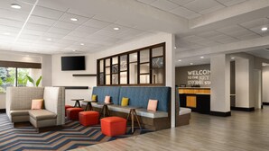 A modern hotel lobby with a seating area, a reception desk, and a large screen. - Hampton Inn Chambersburg (Chambersburg)