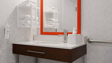 A modern bathroom with a white sink, a mirror with an orange frame, and a towel rack with folded towels.