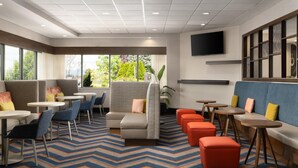 A modern lounge area with seating, tables, and a large window offering a view of greenery. - Hampton Inn Chambersburg (Chambersburg)
