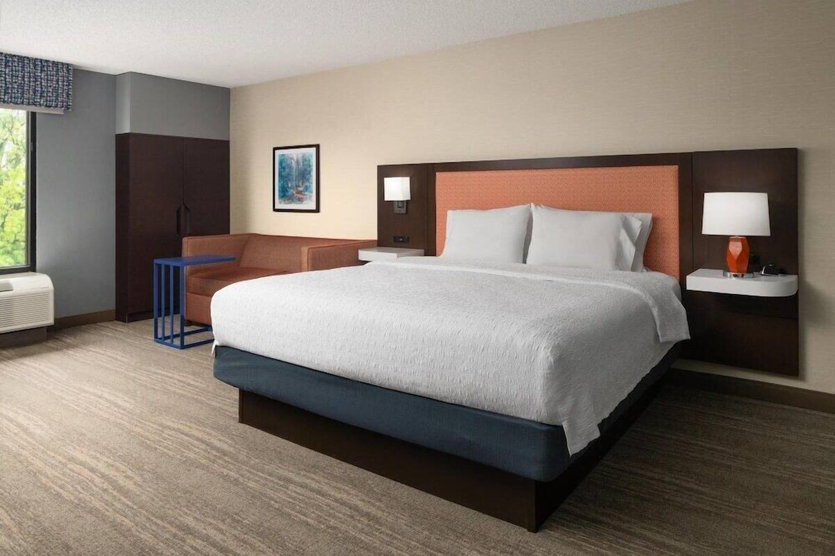 A hotel room with a large bed, a desk, a chair, a nightstand, and a window.