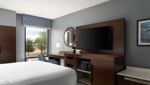 A hotel room with a large bed, a desk with a flat-screen TV, a microwave, and a window with a view of trees. - Hampton Inn Chambersburg (Chambersburg)