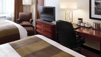 A hotel room with a bed, a desk with a television, a chair, a coffee maker, and a framed picture on the wall.