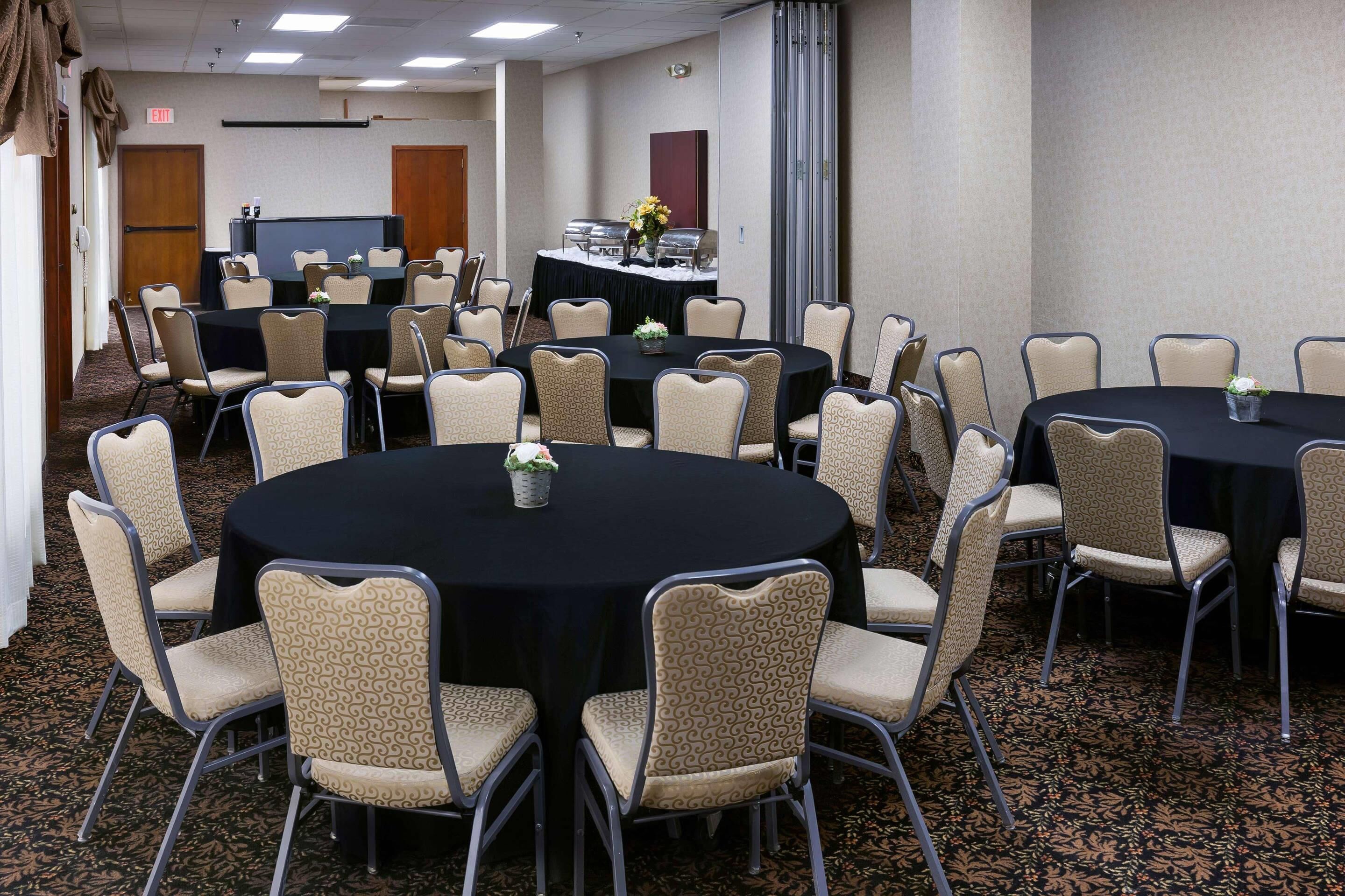 A conference room with round tables and chairs, a projector screen, and a buffet area.