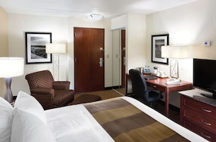 Una habitación de hotel con una cama, un escritorio, una silla, un televisor y una puerta.