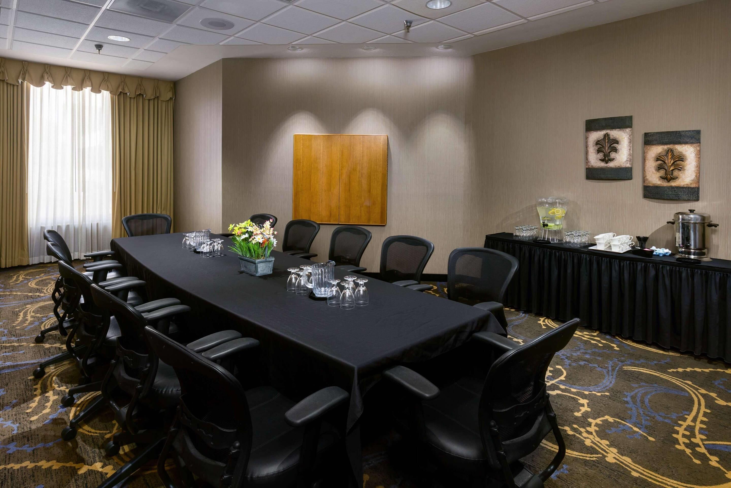 Une salle de conférence avec une longue table, des chaises noires et un sol recouvert de moquette.