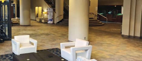 A lobby with a reception desk, white armchairs, a patterned sofa, and a staircase in the background.