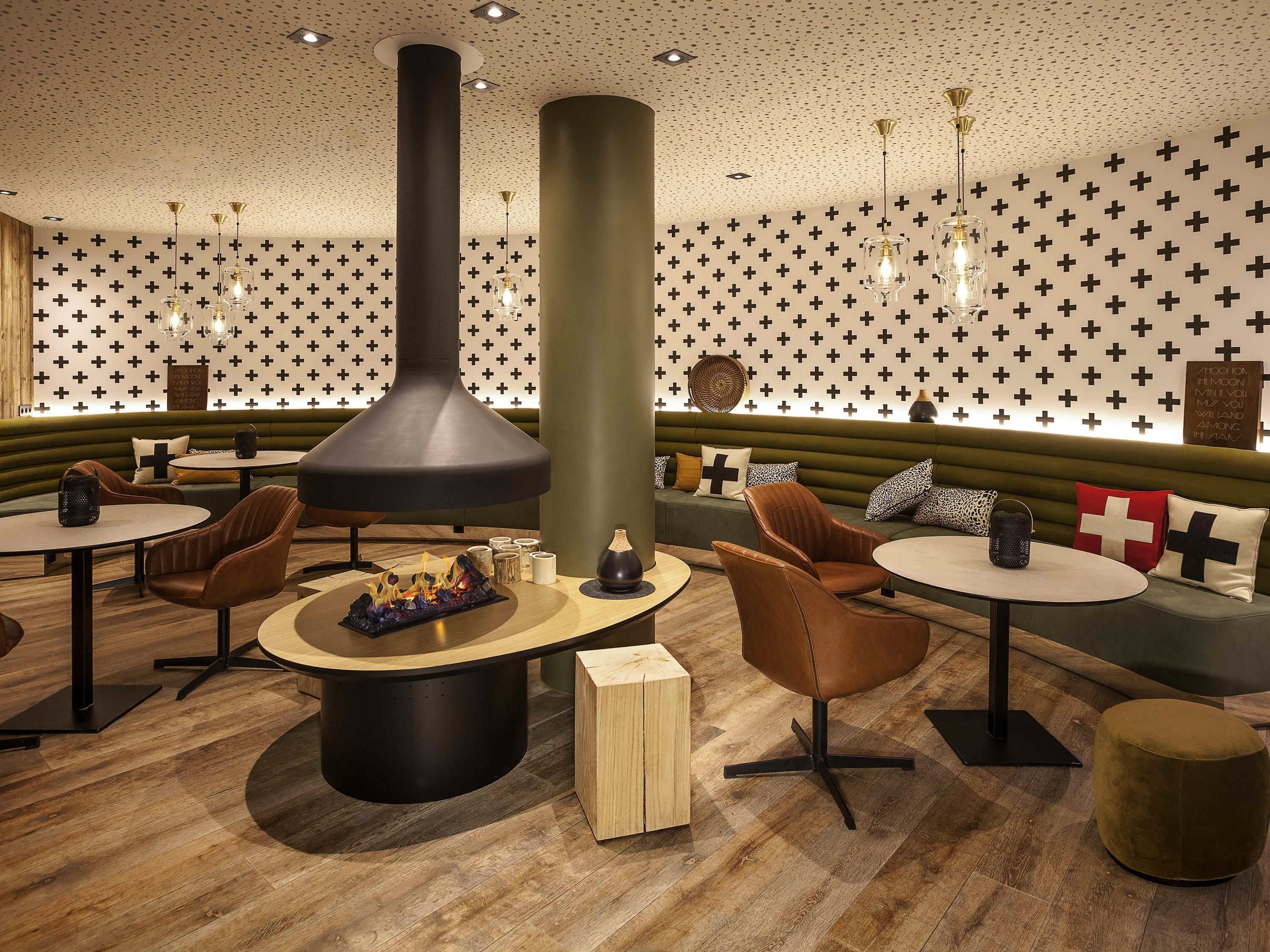 Ein stilvoller Lounge-Bereich mit runden Tischen, Ledersesseln, einem zentralen Kamin und Wandverzierungen.