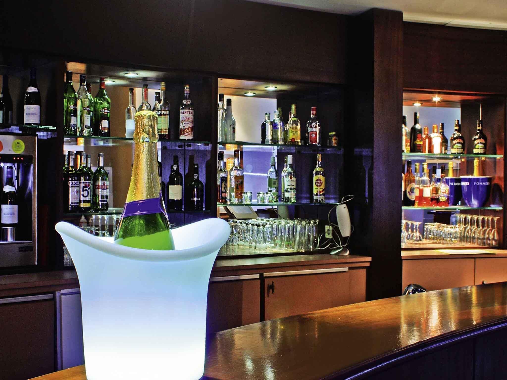A bar area with a bottle of champagne in a white vase, shelves with various liquor bottles, and glasses.