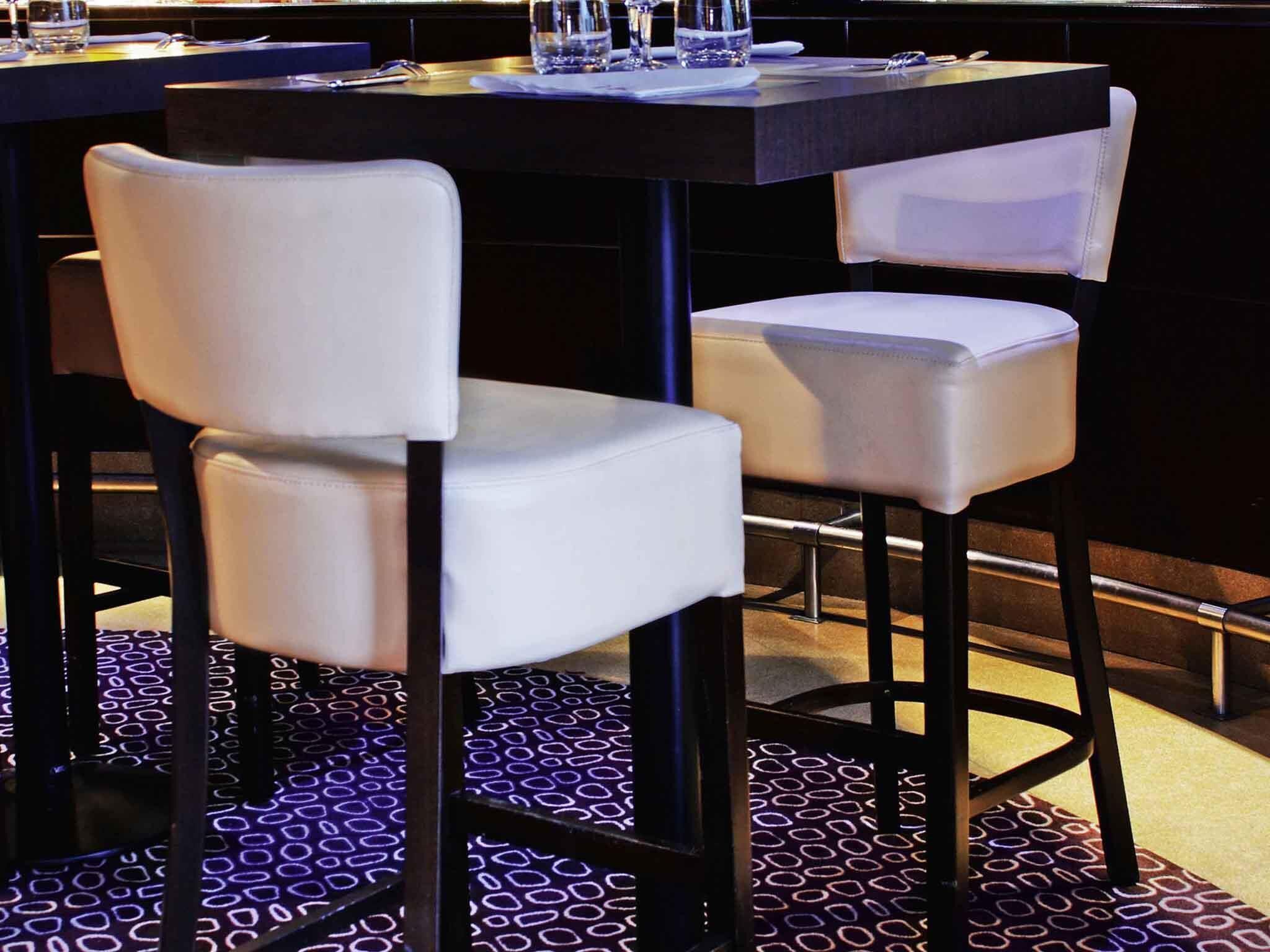 Interior de restaurante con piso oscuro, sillas blancas acolchadas y una mesa negra.