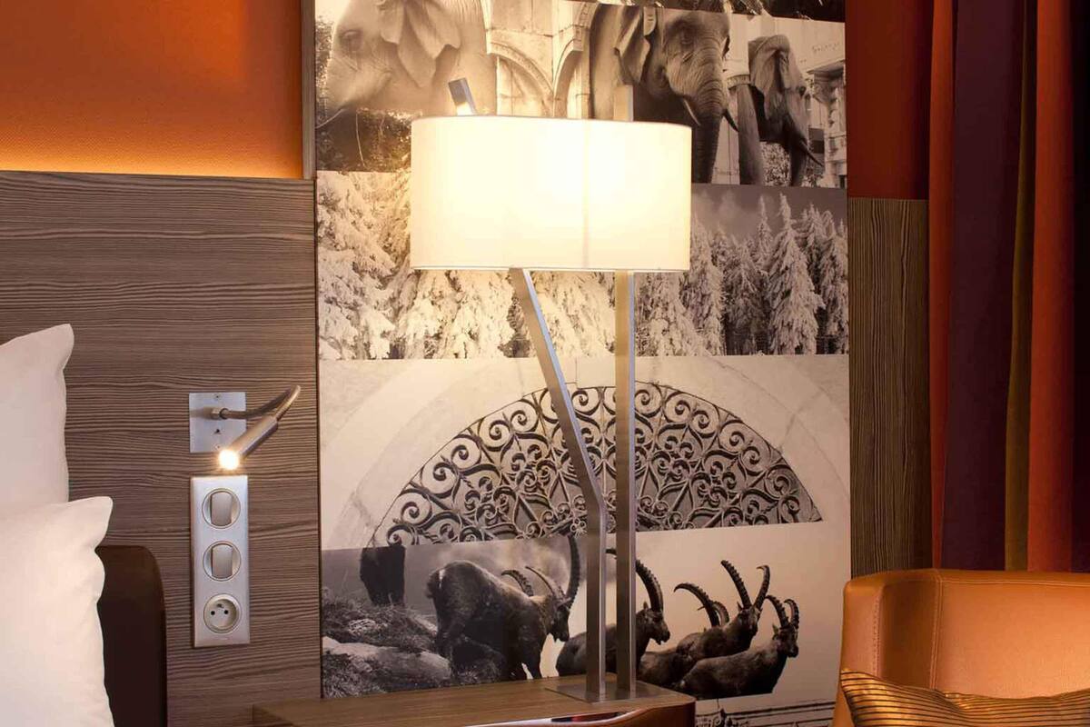 Une chambre d’hôtel comprenant un lit, une lampe, une prise de courant murale et un panneau décoratif mural.