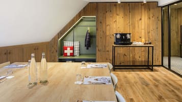 Una sala de reuniones moderna con suelo de madera, una mesa larga con revistas, una máquina de café y un perchero.