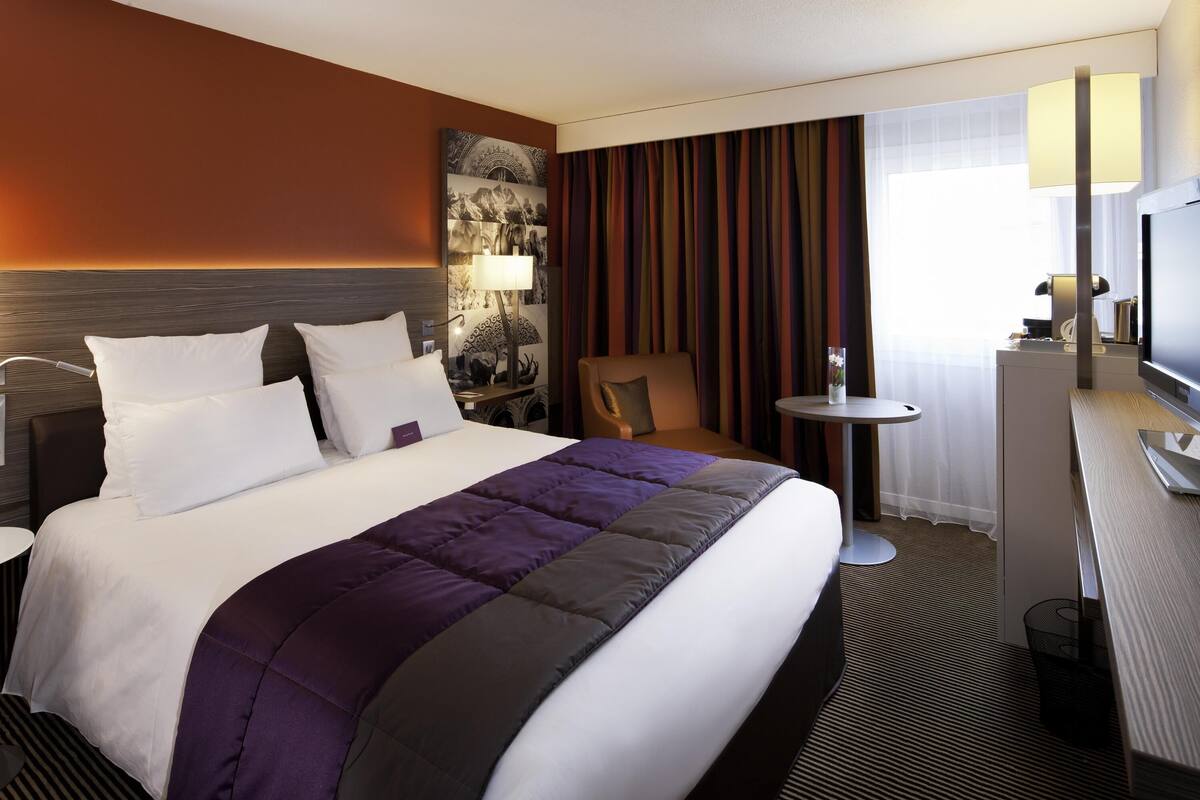 Hotelkamer met een groot bed, een bureau, een stoel, een televisie en een wandlamp.