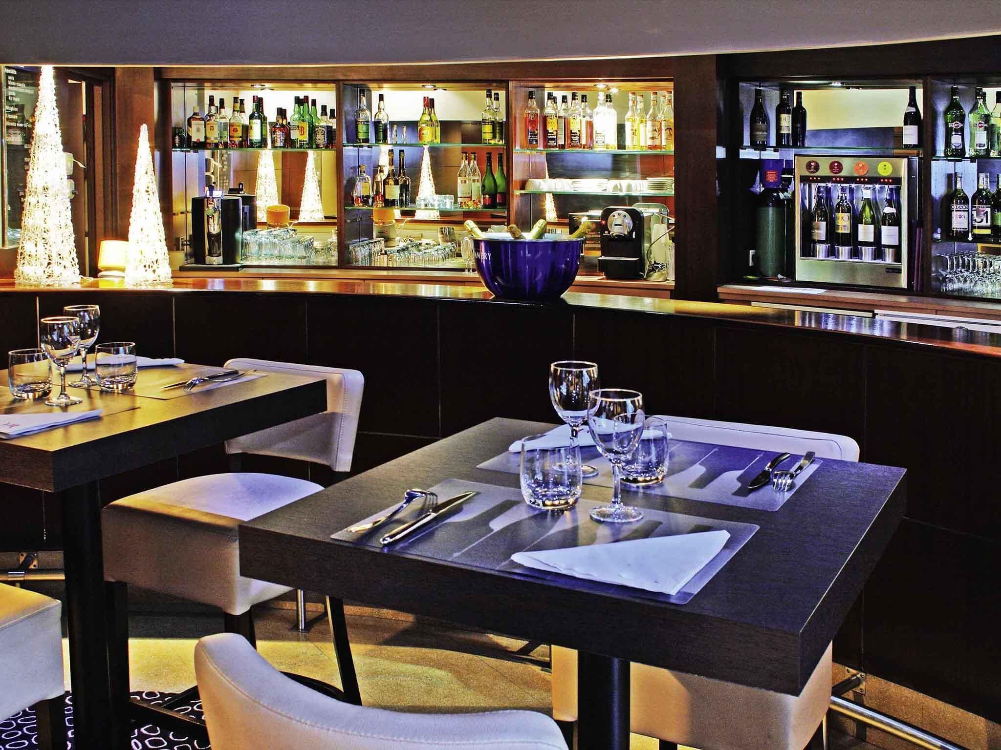 Un área de bar con mesas ordenadas, taburetes y una variedad de botellas y vasos en estantes.