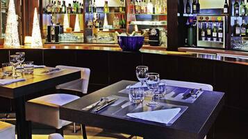 Un área de bar con mesas ordenadas, taburetes y una variedad de botellas y vasos en estantes.