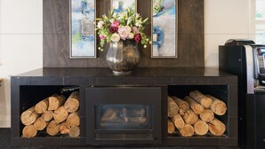 A fireplace with logs, a vase with flowers, and three framed artworks on the wall. - Kiwi International Hotel (Auckland)