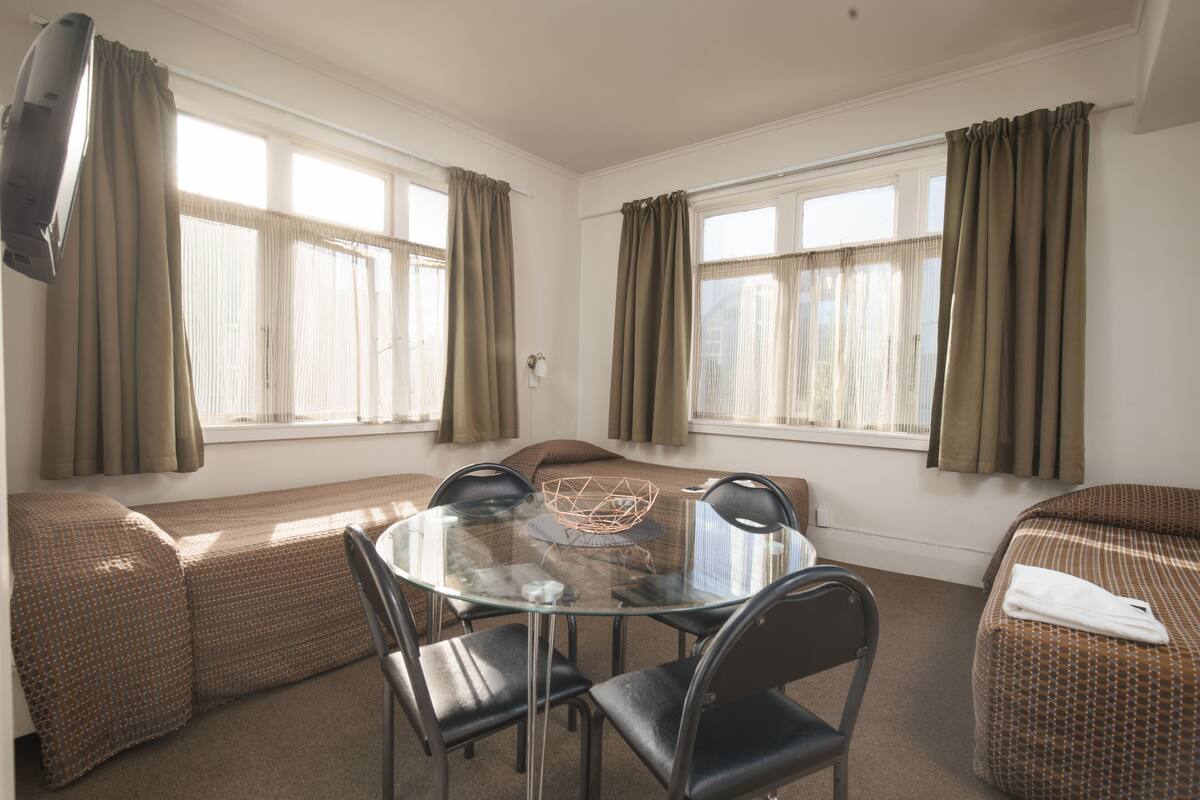 A room with a round glass table surrounded by chairs, a sofa, and a bed.