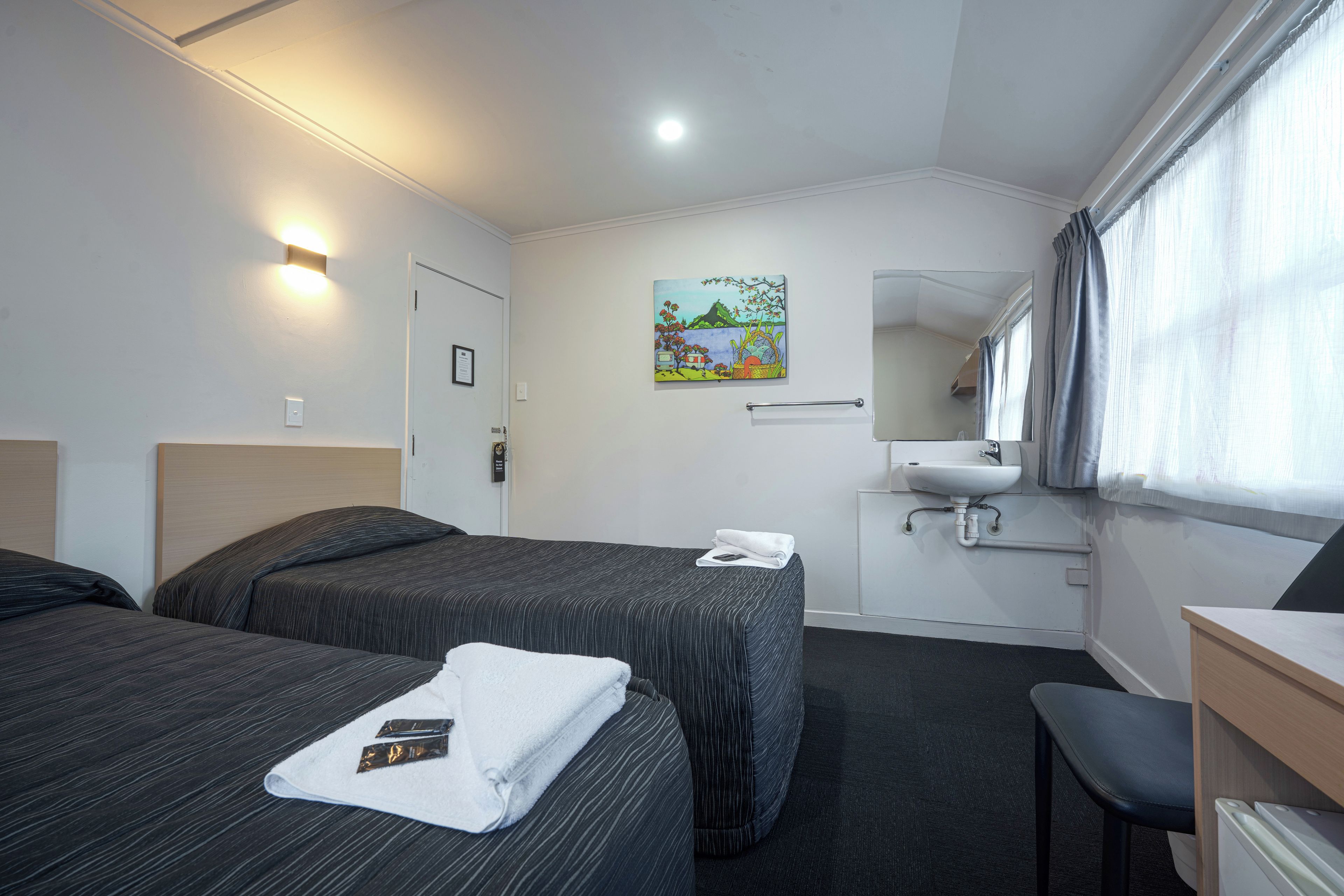 A hotel room with two beds, a bathroom, and a desk.