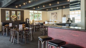 A restaurant with a bar area, wooden tables, and chairs. - Kiwi International Hotel (Auckland)