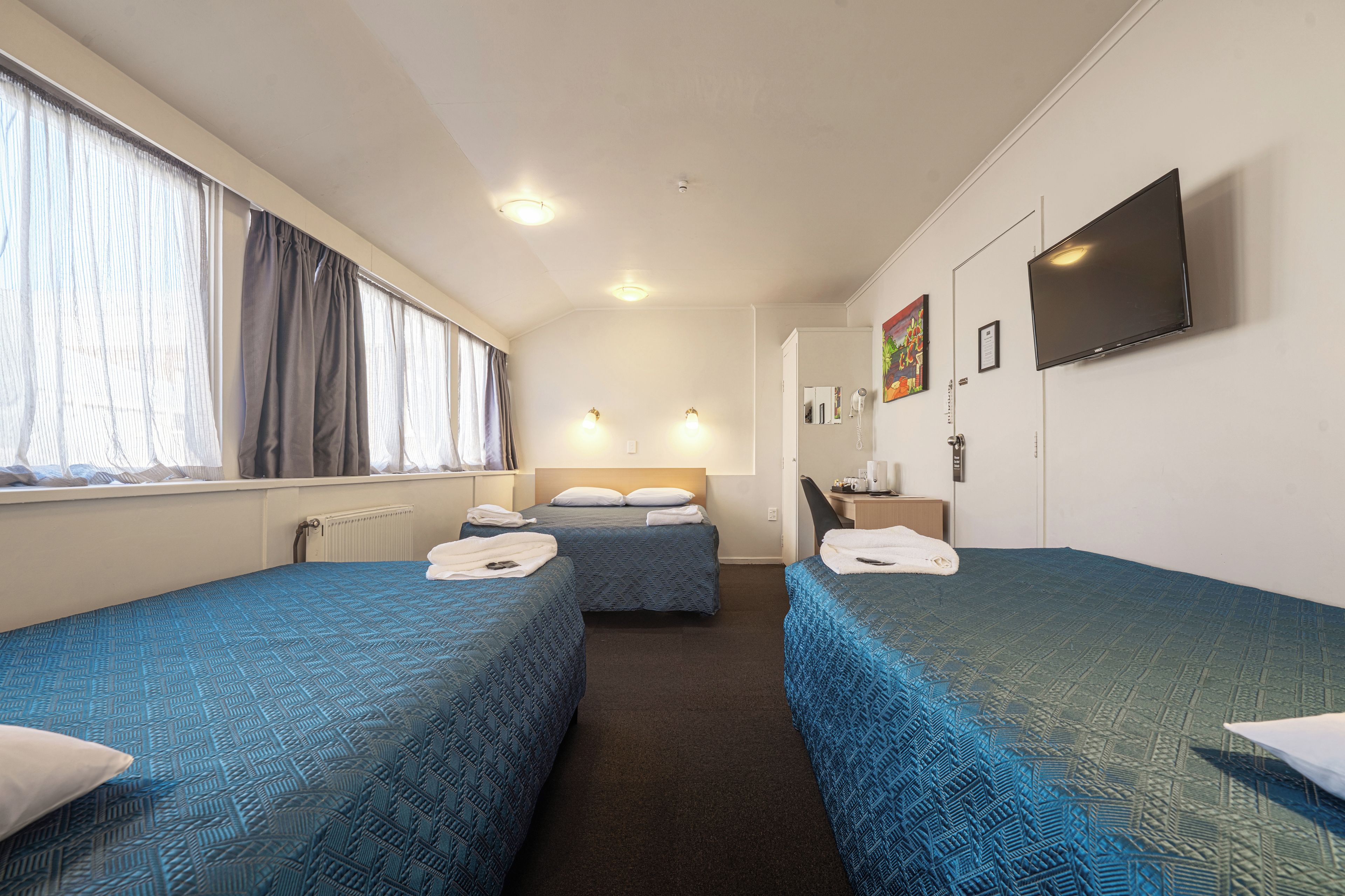 A hotel room with two beds, a TV, a desk, and a window with curtains.
