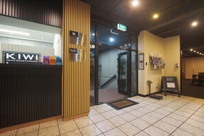A hotel entrance with a wooden panel design, an exit sign, and a reception desk with informational brochures.