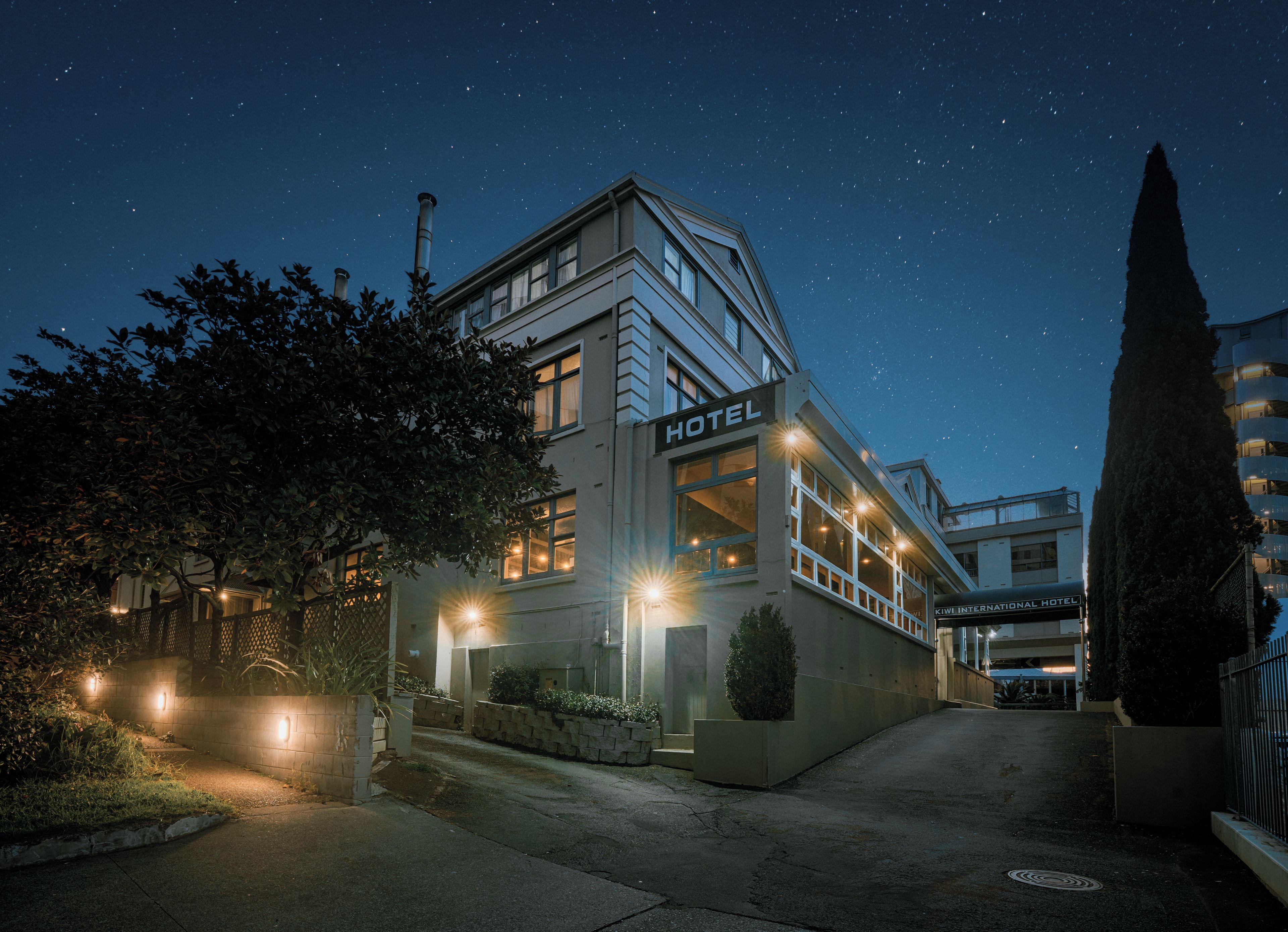 A hotel with a modern design, featuring a prominent 'HOTEL' sign, a well-lit entrance, and a clear night sky.