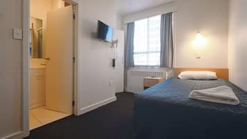 Una habitación de hotel con una cama, un televisor montado en la pared, una ventana con cortinas y un radiador.