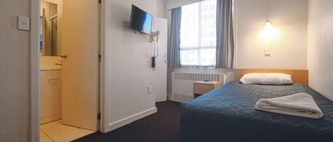 Ein Hotelzimmer mit Bett, Wandfernseher, Vorhängen am Fenster und Heizkörper.