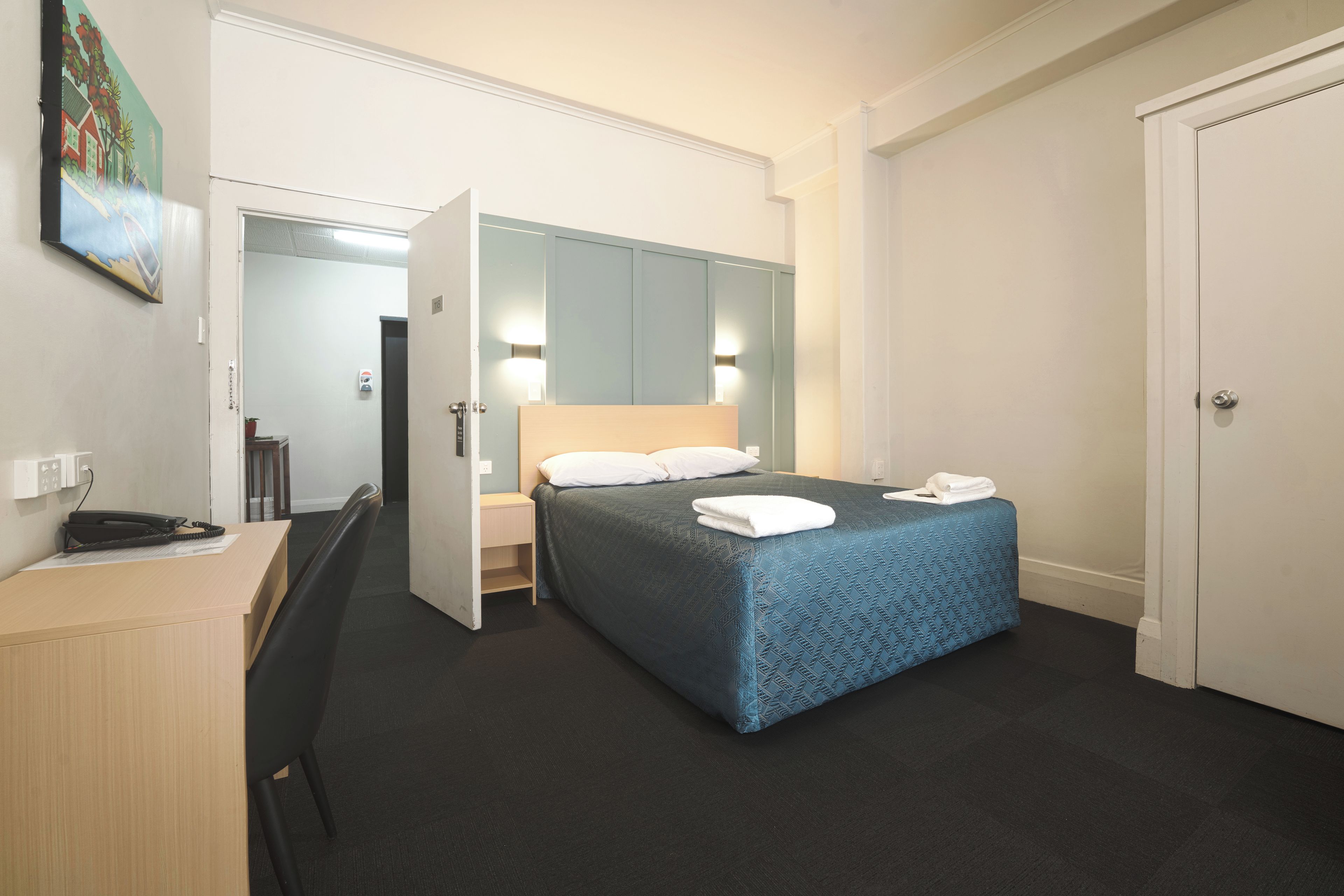 Ein Hotelzimmer mit Bett, Nachttisch und Schreibtisch mit Telefon.